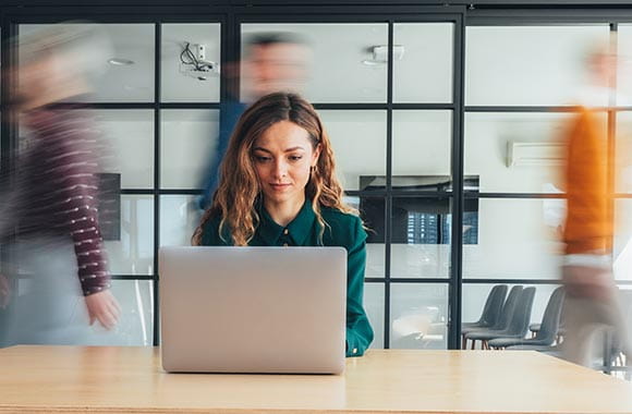 Person on computer with others walking past in backround